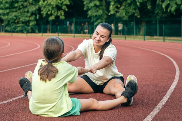 Mother and daughter go in for sports outdoors, caucasian woman and little girl are engaged in fitness at the stadium.