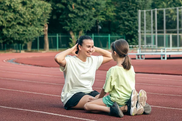 Mother and daughter go in for sports outdoors at the stadium, the girl supports her mom by keeping her company in fitness.
