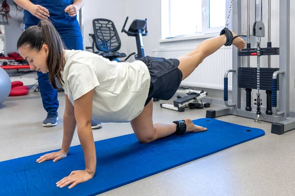 Woman does legs raise exercise to stretch muscles, therapist helping with mechanical disorders in cabinet.