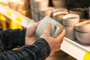 Ev eşyaları dükkanındaki raftan büyük gri bardakları tutan adam..