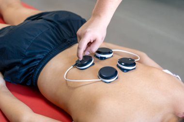 Bir kadın fizik tedavi kliniğinde miostimülasyon tedavisi görüyor. Bir kadına masaj ve rehabilitasyon için myostimülasyon elektrotları takılıyor..