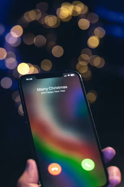 Incoming call screen from Merry Christmas and Happy New Year in hands on a dark blurred background with bokeh.