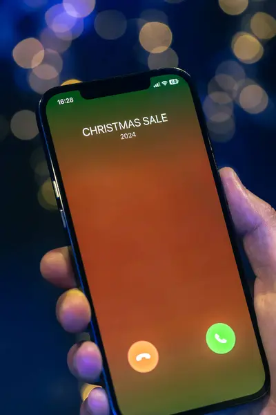 Incoming call screen from Christmas Sale in hands on a dark blurred background with bokeh.