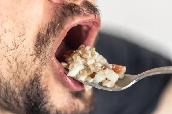 A hungry man opened his mouth, ready to eat a spoonful of porridge with fruit, close-up.