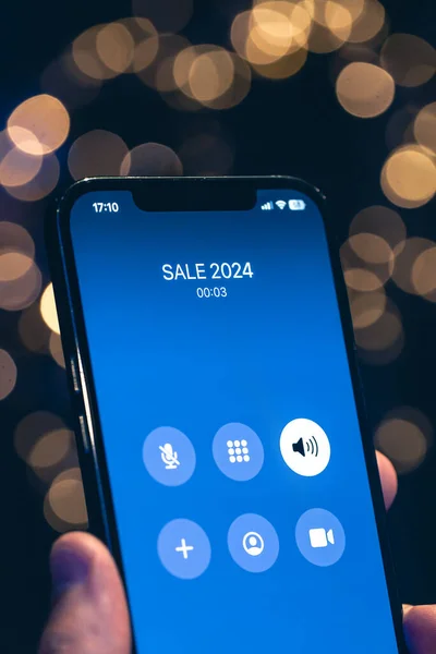 Incoming call screen from Sale 2024 in hands on a dark blurred background with bokeh.