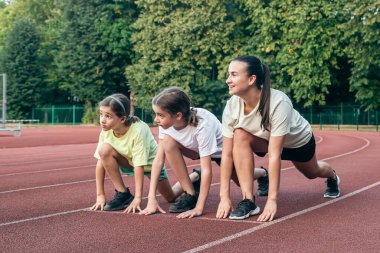 Genç bir kadın ve kız koşucu stadyumda antrenman yaparken koşu pozisyonunda..