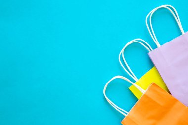 Mavi arkaplanda farklı renkte kağıt torbalar, üst görünüm, alışveriş konsepti, kopyalama alanı.