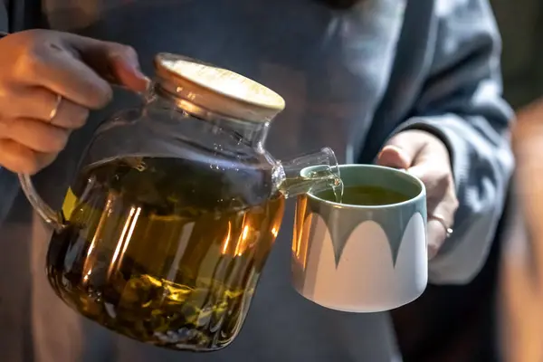 A woman pours tea into a cup late at night, the concept of tea drinking, calming nerves, herbal tea for sleep.