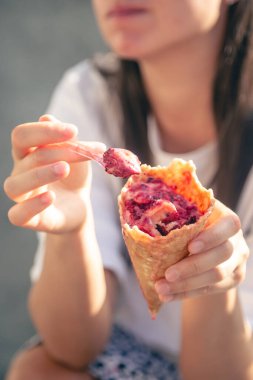 Yakın plan, waffle külahında meyveli dondurma bir kadının ellerinde, bir kadın dışarıda dondurma yiyor..