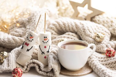 Kış kompozisyonu, bir fincan kakao ve örülmüş bir elementle bulanık bir arka planda marshmallow kardan adam..