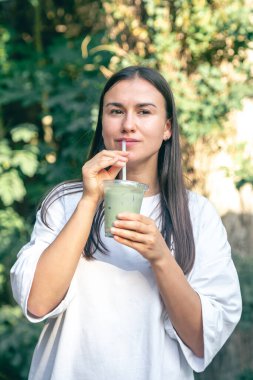 Parkta matcha latte içen şık bir kadın, sağlıklı buzlu içecekle birlikte bir kadın..