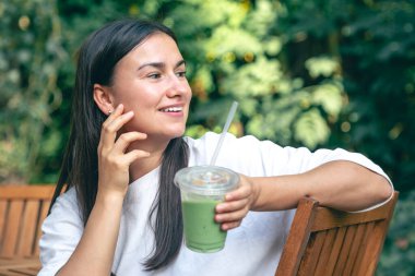 Dışarıdaki kafede oturmuş, Matcha latte içen bir kadın..