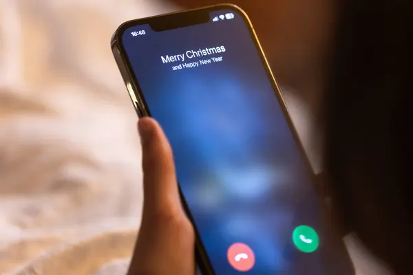 Incoming call screen from Merry Christmas in hands on a blurred background.