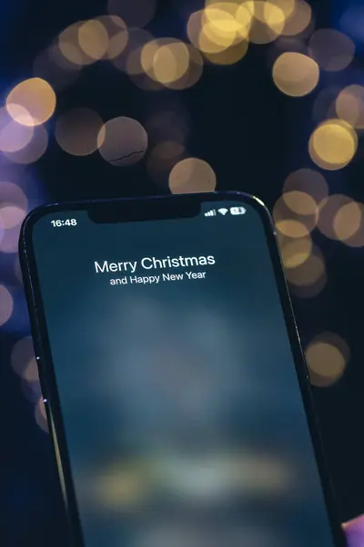 Incoming call screen from Merry Christmas and Happy New Year in hands on a dark blurred background with bokeh.