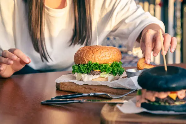 A young woman eating burger in street cafe, close up, american unhealthy calories meal, hungry human with grilled hamburgers.