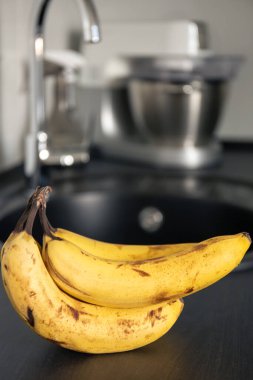 Mutfak masasının üzerinde bir avuç olgun sarı muz mutfak musluğunun bulanık arka planına karşı..