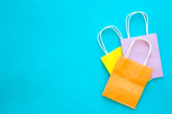Paper bags of different colors on a blue background, top view, shopping concept, copy space.