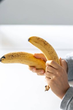 Beyaz bulanık bir arka planda iki olgun sarı muz, kadınların ellerinde..