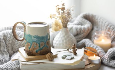 Bir fincan, kitaplar, mumlar ve İskandinav tarzında örülmüş bir element ile rahat bir sonbahar kompozisyonu..