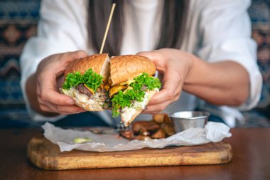 Yakın plan, kafede bir kadın elinde et ve marullu iştah açıcı bir burger tutuyor..