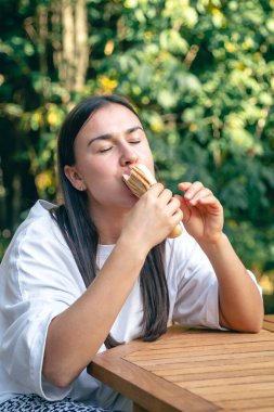 Genç bir kadın sosisli sandviçi bir kafede iştah açıcı bir şekilde yer, sokak fast food konsepti..