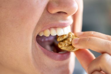 Bir kadının detaylı görüntüsü cevizi ısırır, yakından..