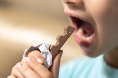 Bir kızın detaylı fotoğrafı çikolatayı ısırıyor, yakın plan..