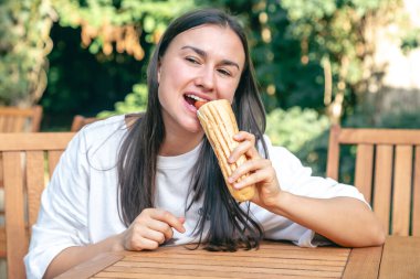 Genç bir kadın sosisli sandviçi bir kafede iştah açıcı bir şekilde yer, sokak fast food konsepti..