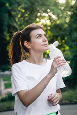 Açık havada egzersiz yaptıktan sonra su içen çekici genç kadın, koşu konsepti..