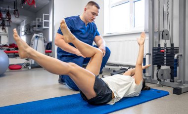 Kadın yoga minderinde yatıyor ve genç fizyoterapistinin yardımıyla jimnastik yapıyor. Yaralı insanlar için fizik tedavi kavramı..