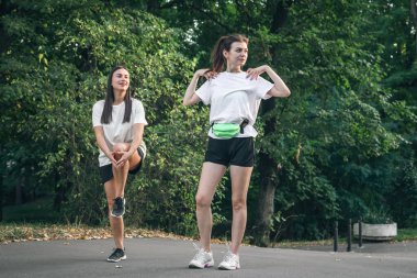 Parkta koşmadan önce kaslarını ısıtmak için egzersiz yapan iki genç kadın..