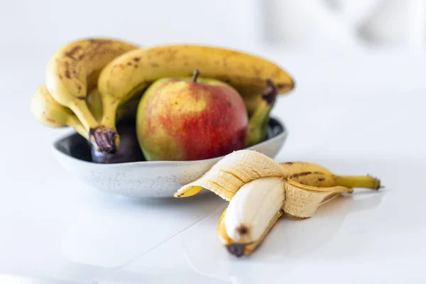An open banana and a plate of fruit on the kitchen table, close up.