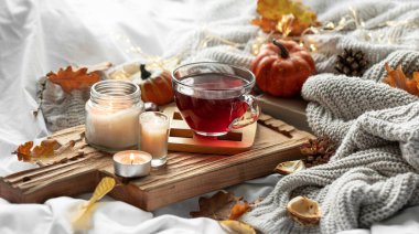 Bir fincan çay, mum, yaprak ve bulanık arkaplanda örülmüş bir elementle sonbahar kompozisyonu.