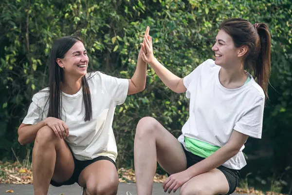Two female friends high-five each other after jogging in the park, outdoor workout concept.