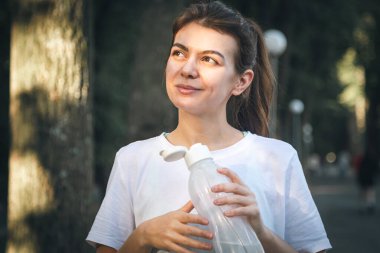 Parkta koştuktan sonra elinde bir şişe suyla mutlu bir genç kadın..