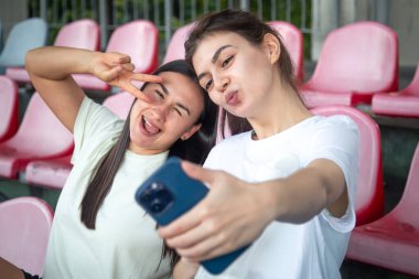 Stadyumdaki eğitimden sonra tribünde akıllı telefonla selfie çeken neşeli atletik genç kadınlar..