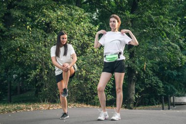 Parkta koşmadan önce kaslarını ısıtmak için egzersiz yapan iki genç kadın..