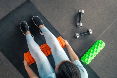 Kadın baldır kaslarının bağcıklarıyla çalışıyor. Spor salonunun zemininde bir masaj köpüğü var..