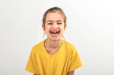 Sarı tişörtlü küçük bir kız izole edilmiş beyaz bir arka planda neşeyle gülüyor..