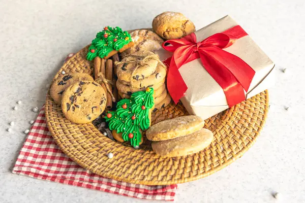 Festive Christmas cookies and gift box in a wicker plate on the kitchen table, homemade baked goods.