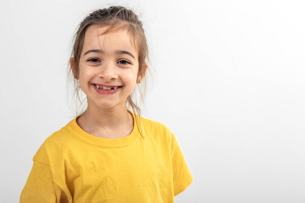 Portrait of a happy little Caucasian girl in a yellow T-shirt on a white background isolated, child smiling with teeth, copy space.