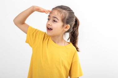 Sarı tişörtlü küçük bir kız, alnının yanında el ele tutuşuyor, uzaklardan beyaz arka planda izole edilmiş uzaklara bakıyor..