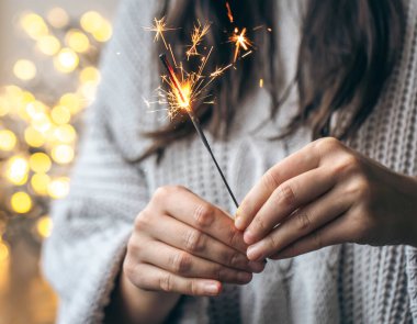 Elinde parlak bir maytap tutan gri kazaklı kadın arka planda bulanık, yakın plan, Noel kutlaması konsepti..