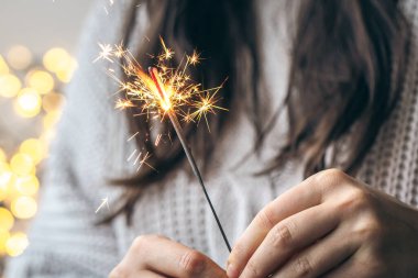 Elinde parlak bir maytap tutan gri kazaklı kadın arka planda bulanık, yakın plan, Noel kutlaması konsepti..