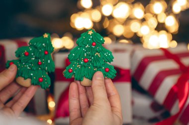 Zencefilli Noel kurabiyeleri, kadınların elinde köknar ağacı şeklinde, hediye kutularının arkasında, Noel kutlaması konsepti..