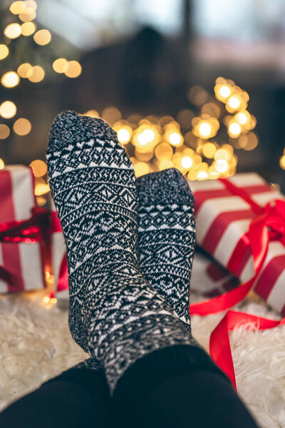 Feet in Christmas socks and gift boxes in front of the fireplace, close up, relaxing at home, cozy background.