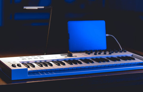 Musical keys and tablet in a dark room. Home music studio. Working with sound.