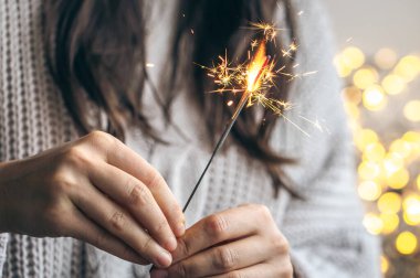 Elinde parlak bir maytap tutan gri kazaklı kadın arka planda bulanık, yakın plan, Noel kutlaması konsepti..