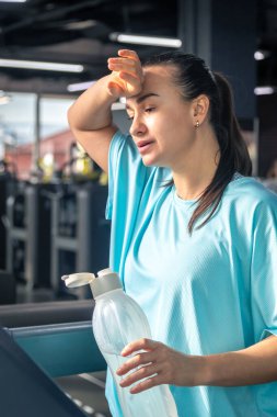 Spor salonunda koşu bandında kardiyo çalışmasından sonra su içen bir kadın..