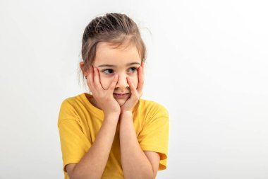 Sarı tişörtlü küçük beyaz bir kız başını tutuyor, zor bir sorunu çözüyor, beyaz arka plandaki sorunu nasıl çözeceğini düşünüyor, izole edilmiş bir şekilde..
